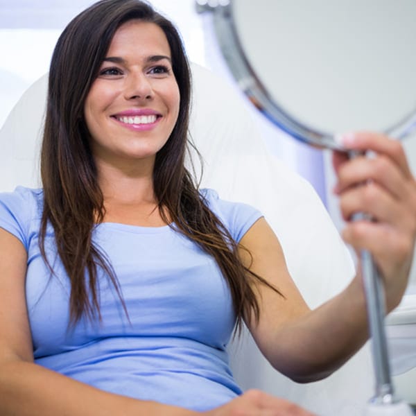 Smiling female patient checking her smile design results in a mirror at a dental clinic in Colombia